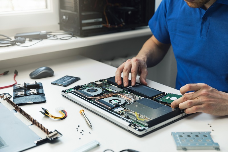 Ein Mann justiert die Hardwarekomponenten eines teilweise zerlegten Laptops auf einem Tisch vor ihm.