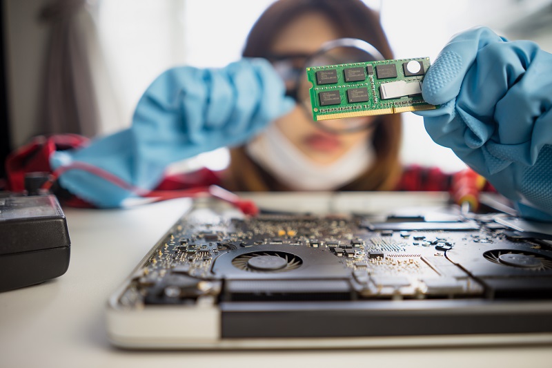 Eine Computertechnikerin untersucht mit Hilfe einer Lupe eine Leiterplatte mit einigen Prozessorchips.