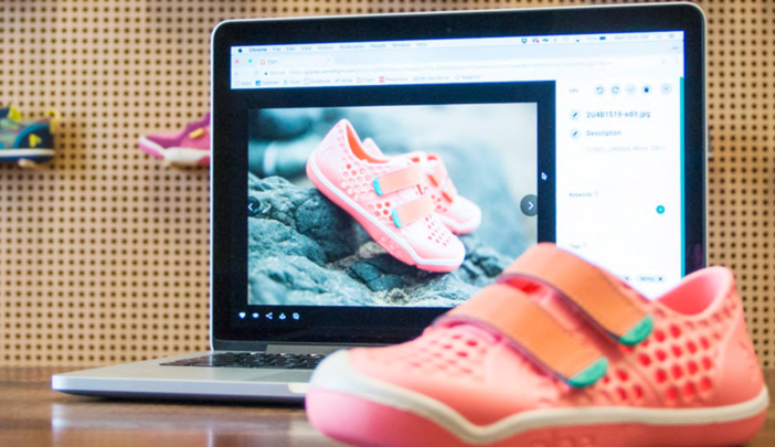 Ein Paar Kinderschuhe neben einem Laptop, der dasselbe Paar Kinderschuhe auf einer Webseite zeigt.