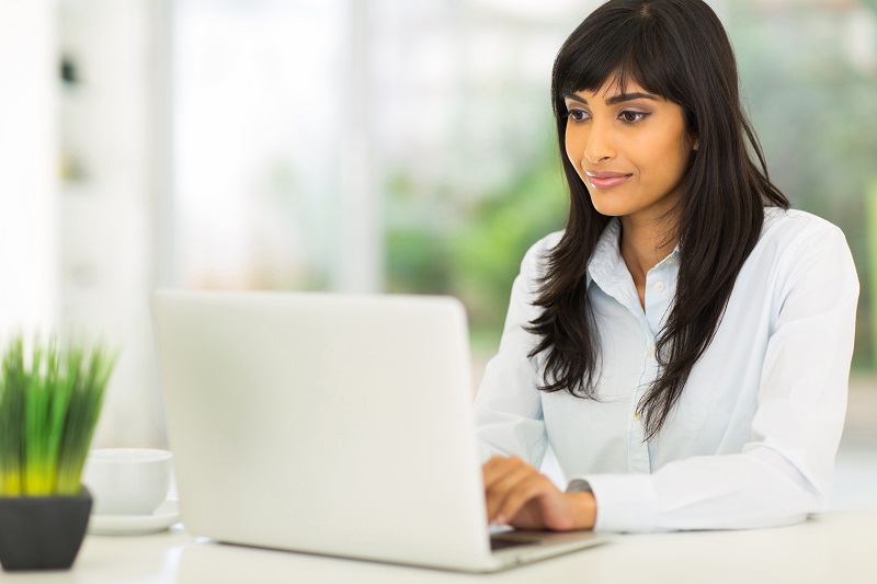 Eine junge Frau arbeitet an ihrem Schreibtisch sitzend mit ihrem Laptop.