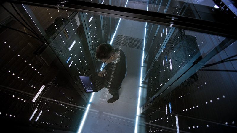 Ein Mann überprüft die Server in einem Rechenzentrum mit Hilfe seines Laptops.