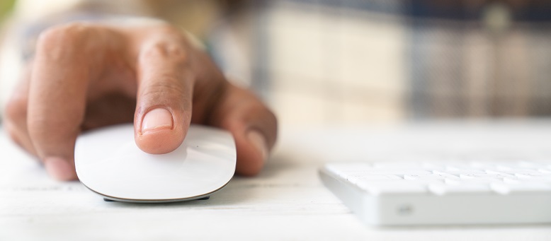 Die Hand eines Mannes, der eine Computermaus bedient, die sich neben einer Tastatur auf einem Tisch befindet.