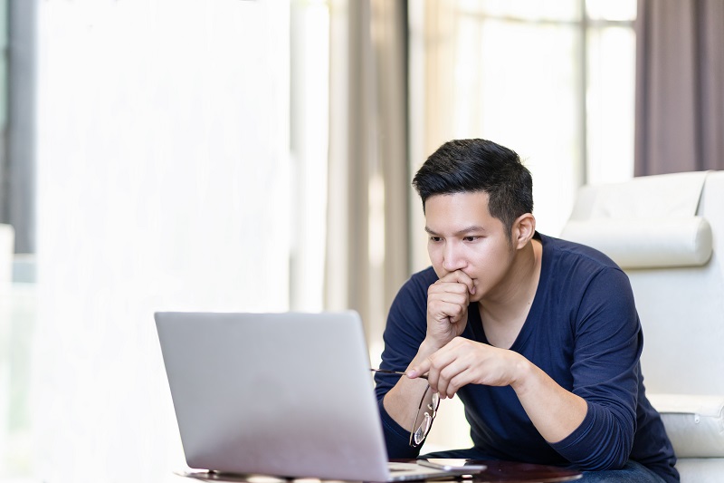 Ein junger Mann sitzt vor einem Laptop und betrachtet ihn sehr konzentriert.