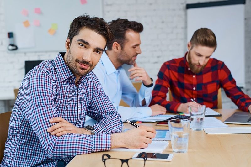 Drei junge Männer sitzen gemeinsam an einem Bürotisch und arbeiten zusammen.