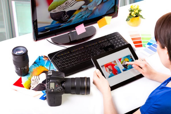 Eine Grafikdesignerin sitzt an einem PC und entscheidet mit einem Tablet, welches Bild sie auswählen soll.