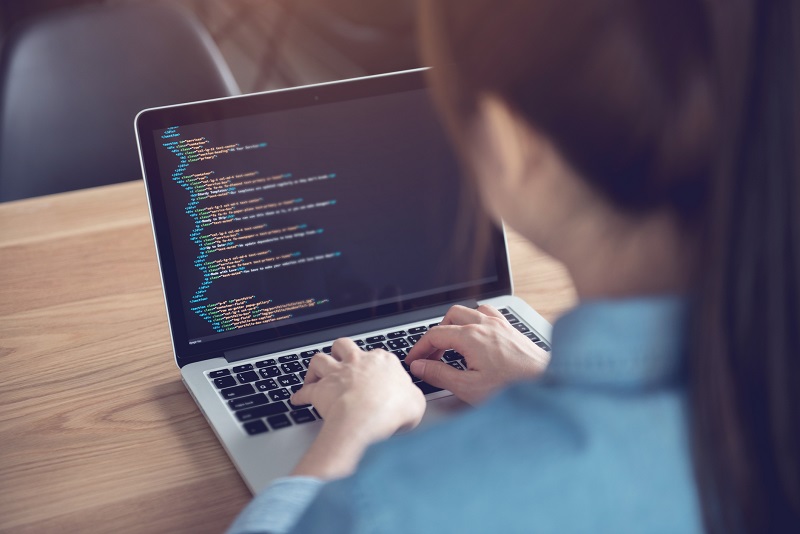 Eine Frau verwendet ihren Laptop, um Code für eine Datei im Dokument-Dateityp HTML zu programmieren.