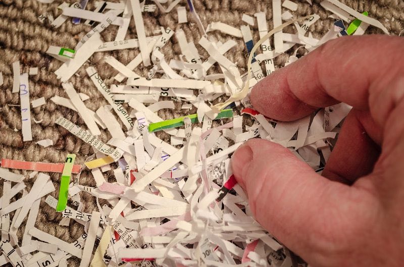 Eine Hand sammelt Schnipsel aus einem Haufen geschredderten Papiers.