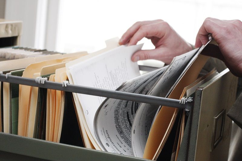 Eine Abbildung von Händen, die in einem Aktenschrank verschiedene Papiere durchgehen.