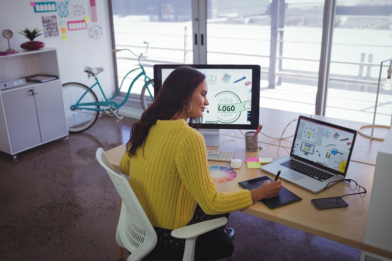 A designer using both a laptop and computer to edit images.