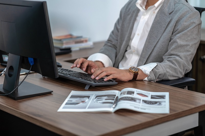 A worker types on a keyboard while referring to a magazine.